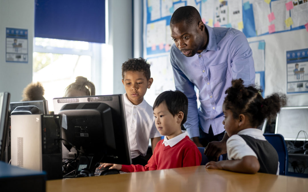 Male teacher supporting technology curriculum in computer classroom with students looking at computer screen