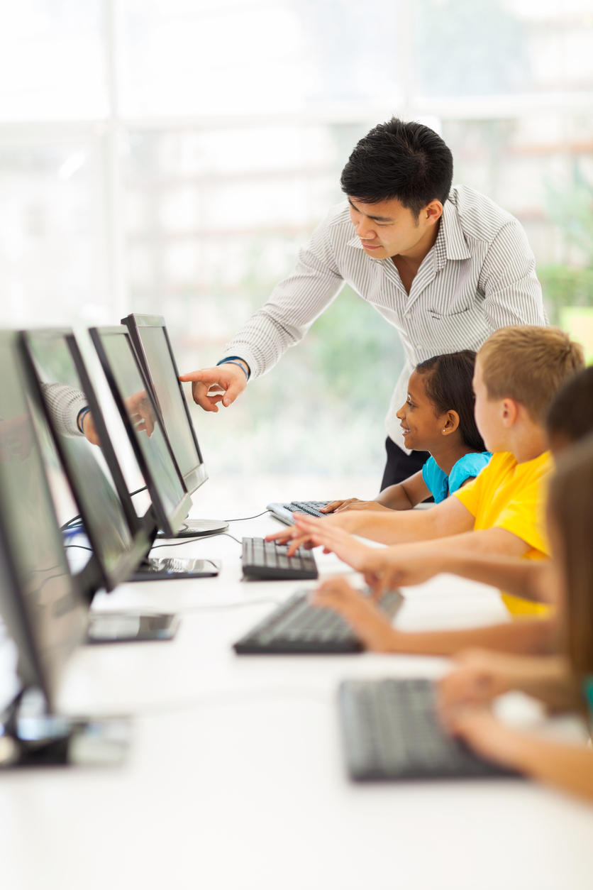 Teacher helping elementary students learn computer fundamentals in computer room
