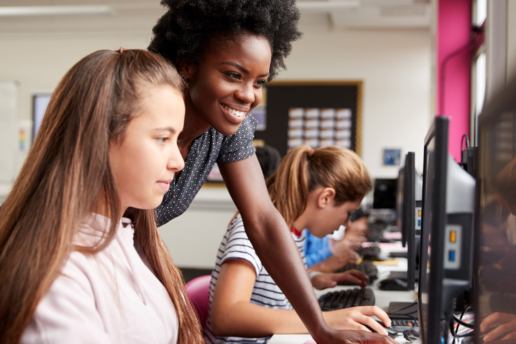 Two young female students thinking like programmers on a laptop in a classroom