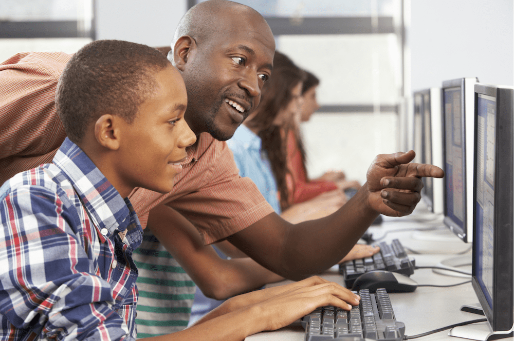 Student with teacher supporting digital literacy skills in classroom